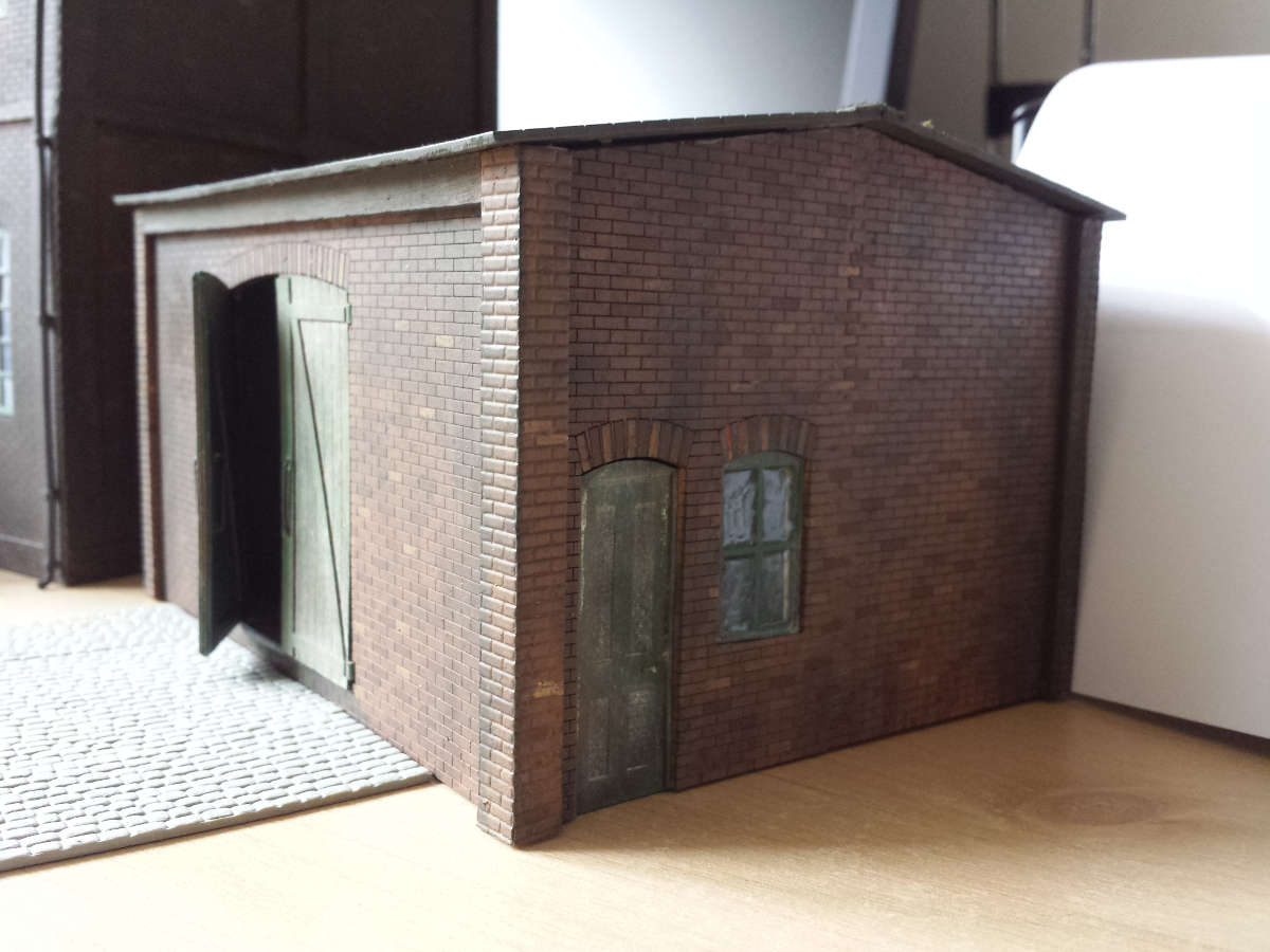 An exceptionally well finished goods shed in O gauge by Steve Farrands. Comment from Steve: "The main building was constructed as a full relief building. I did not use the upper floor opening, which I adapted into making a vehicle workshop to go at the side of the warehouse. I had pictures of a particular warehouse I wanted to model and using colour photographs of the actual building I made the main unit. The windows were adapted by cutting out the middle frame and once glazed the open part was added to the main frame. The glazing was ordinary wood glue dragged across the panes using a cocktail stick. Some panes had dried broken but I think they look very realistic for broken panes of glass. I added guttering and downpipes as well."